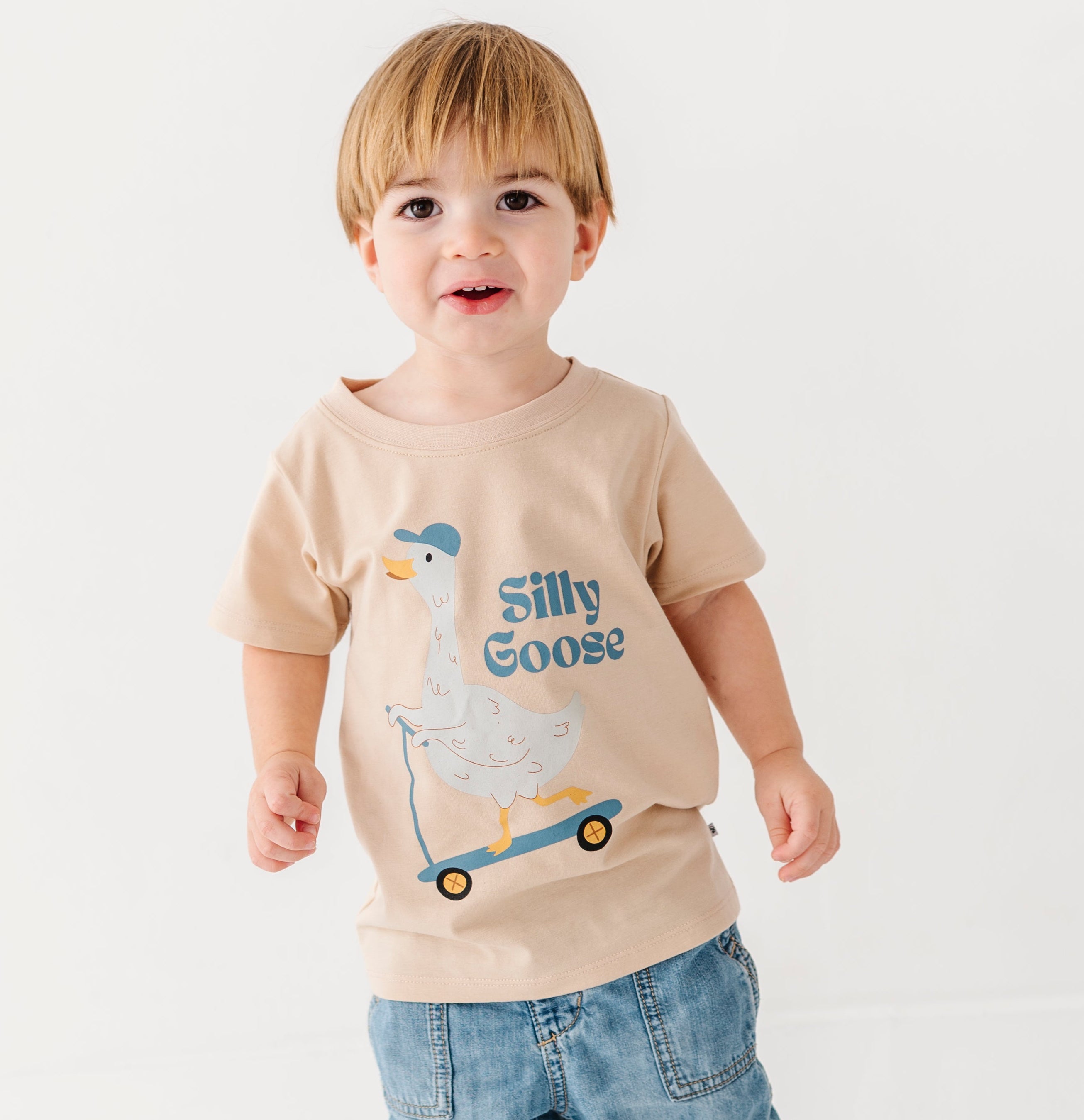 Child wearing a beige t-shirt with a silly goose graphic design and text, standing on a white background